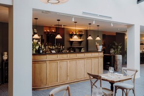 Un espace bar agrémenté de meubles en bois, de luminaires suspendus et d’un coin salon avec des tables et des chaises.