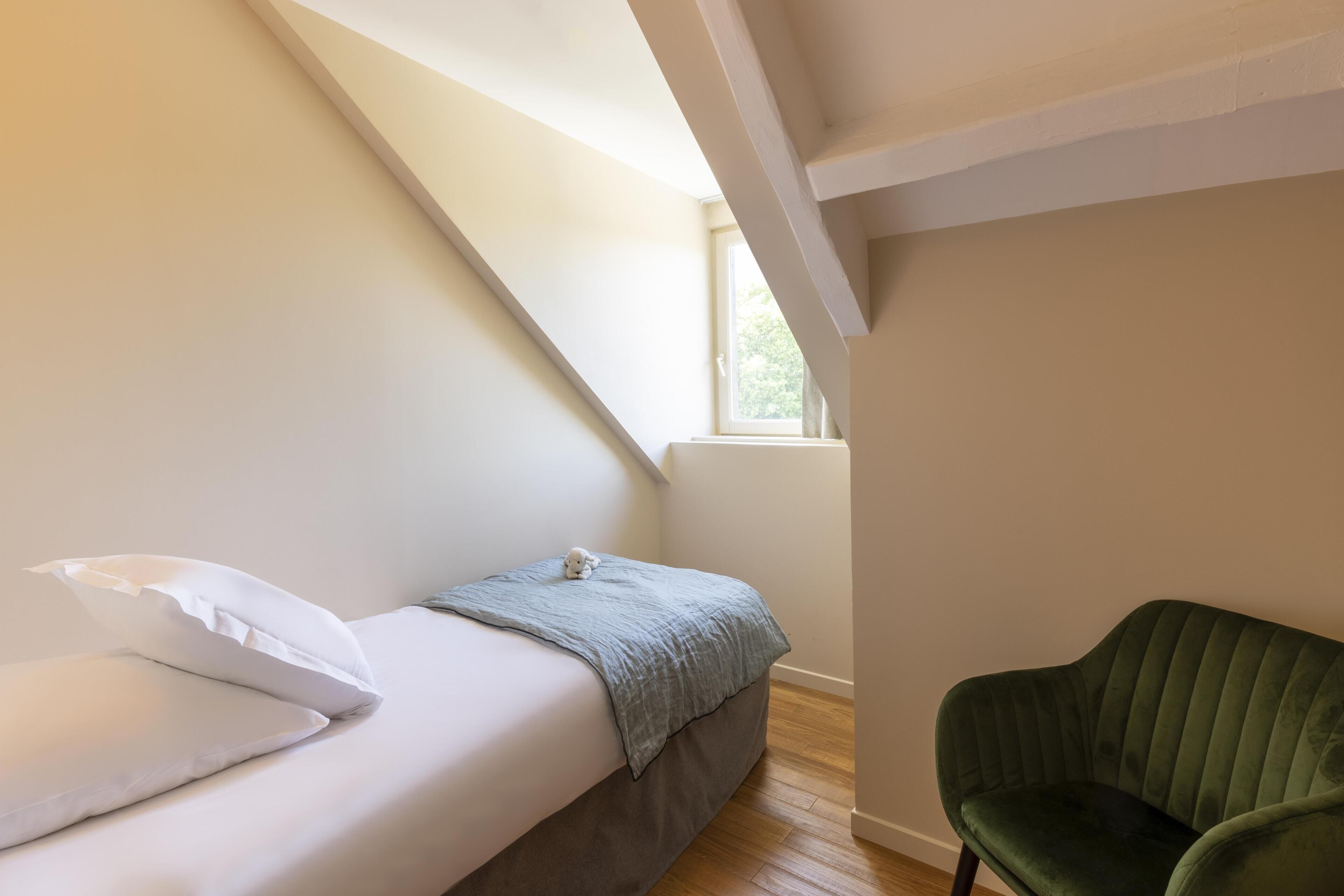 A bedroom with a bed, pillows, a green chair, and a window.