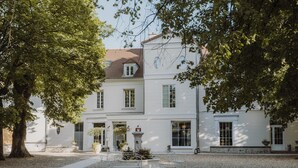 Un edificio blanco de dos pisos con un patio de grava, una fuente y un árbol.