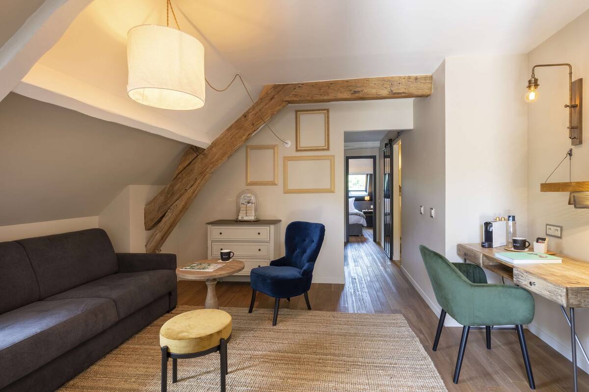 Un appartement-loft chaleureux avec un canapé gris foncé, un fauteuil bleu, un bureau en bois et un luminaire suspendu.
