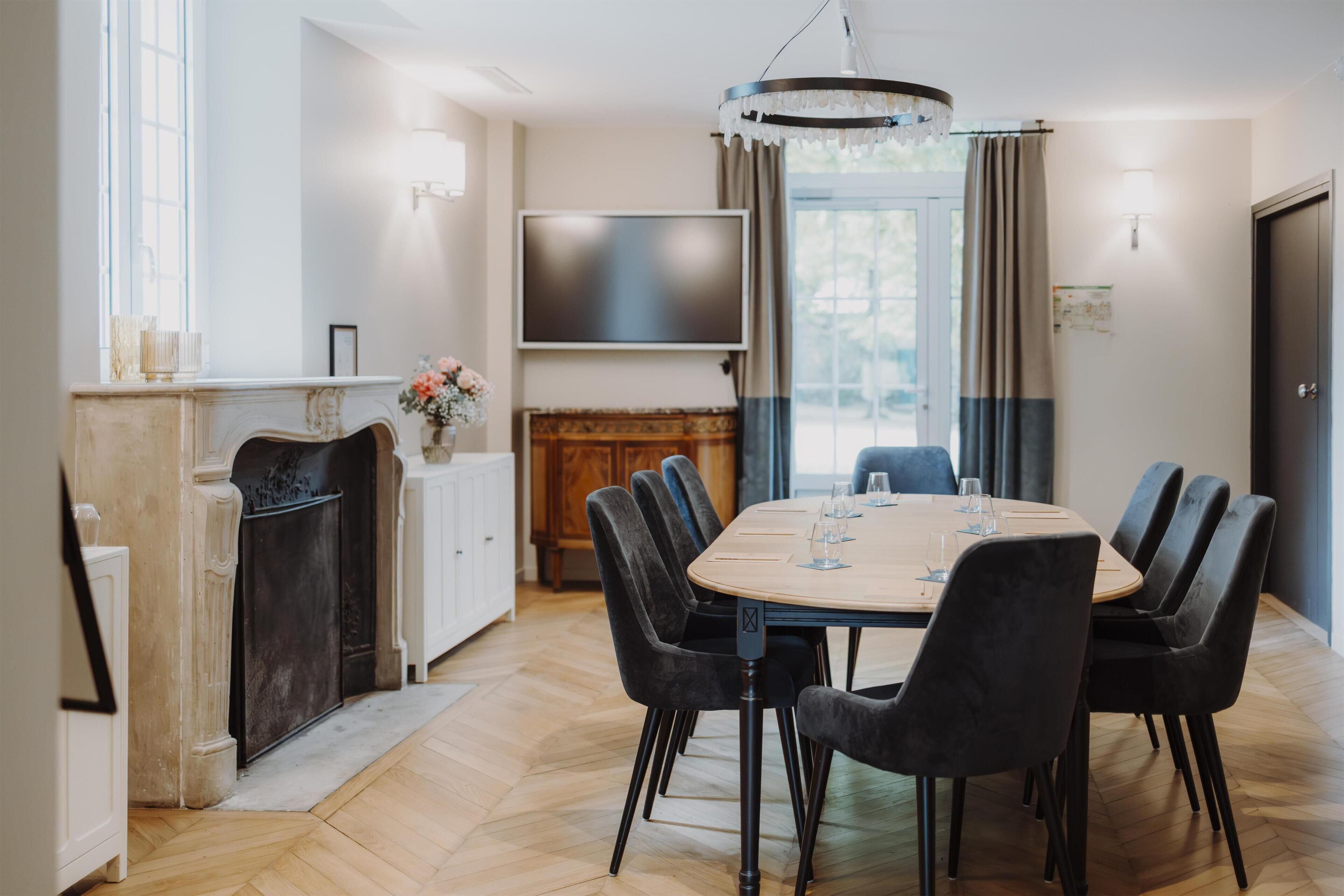 A dining area with a round table, chairs, a fireplace, a TV, and a chandelier.