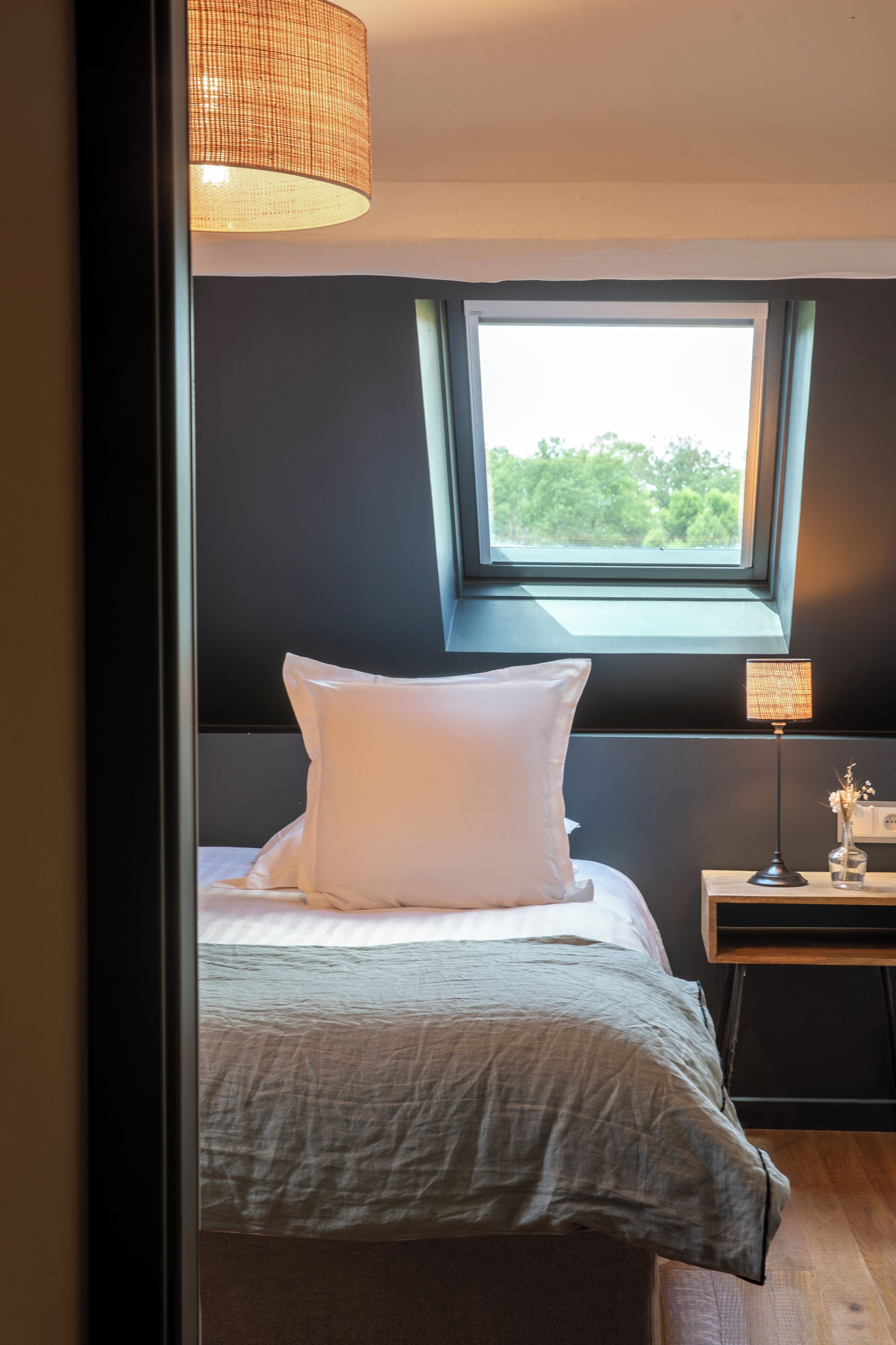 Ein Schlafzimmer mit Bett, Fenster, Nachttisch und Lampe.