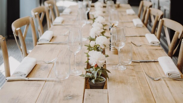 Una larga mesa de madera con sillas, dispuesta para comer, y lámparas con flecos dorados colgando arriba.