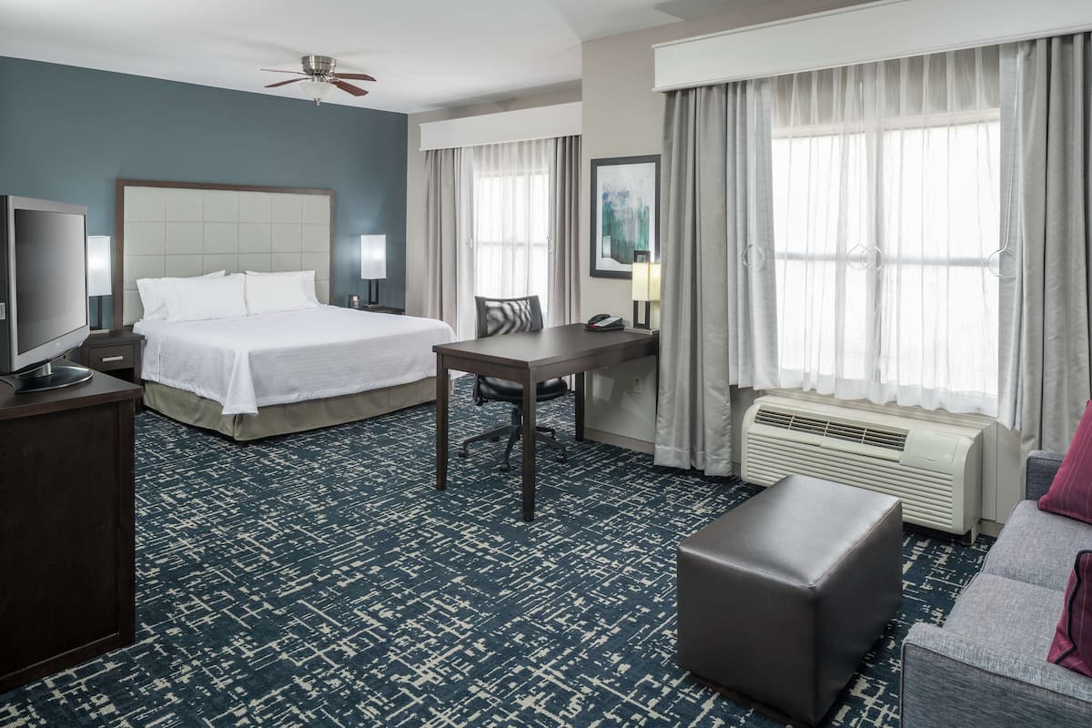 A hotel room with a bed, desk, chair, television, and a sofa.