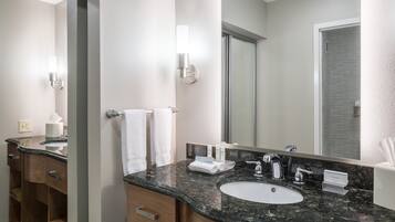 A modern bathroom with a granite countertop sink, a large mirror, and a towel rack.
