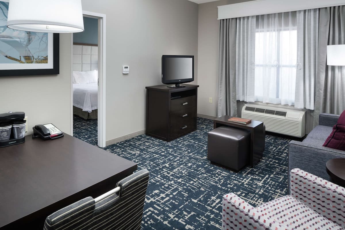 A hotel room with a bed, a desk with a telephone, a television on a cabinet, a sofa, and a window with curtains.