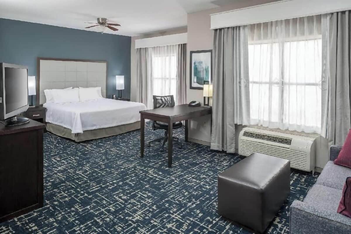 A hotel room with a bed, desk, chair, TV, and a sofa.