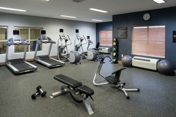 A gym with treadmills, elliptical machines, a bench, dumbbells, and exercise balls.