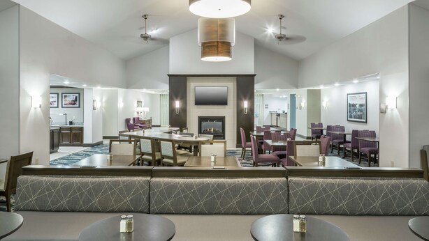 A modern hotel lobby with a central seating area, multiple dining tables, and a fireplace. - Homewood Suites by Hilton Cedar Rapids-North (Cedar Rapids)