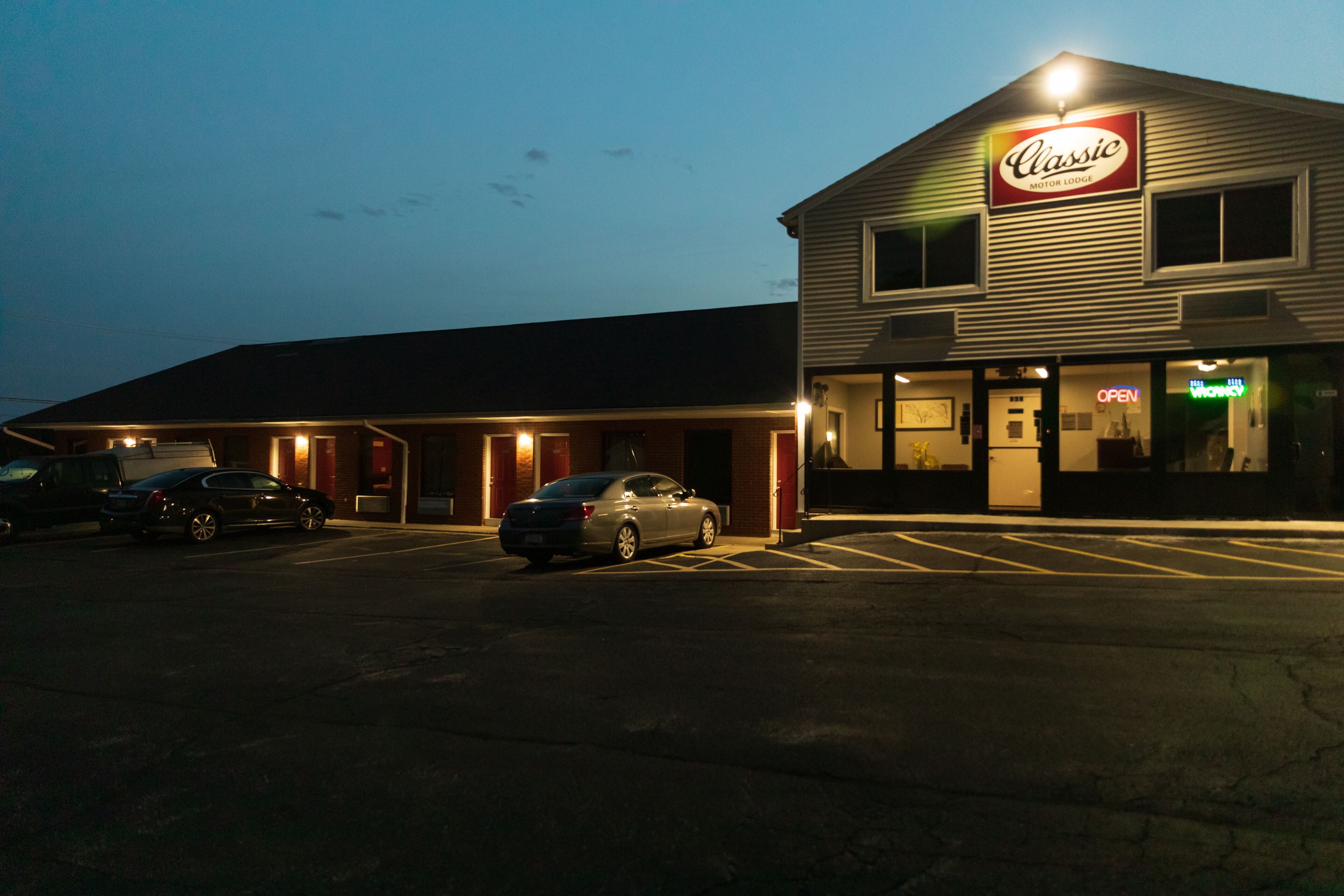 A Classic Motor Lodge with a parking lot, a car parked in front, and a building with a sign.