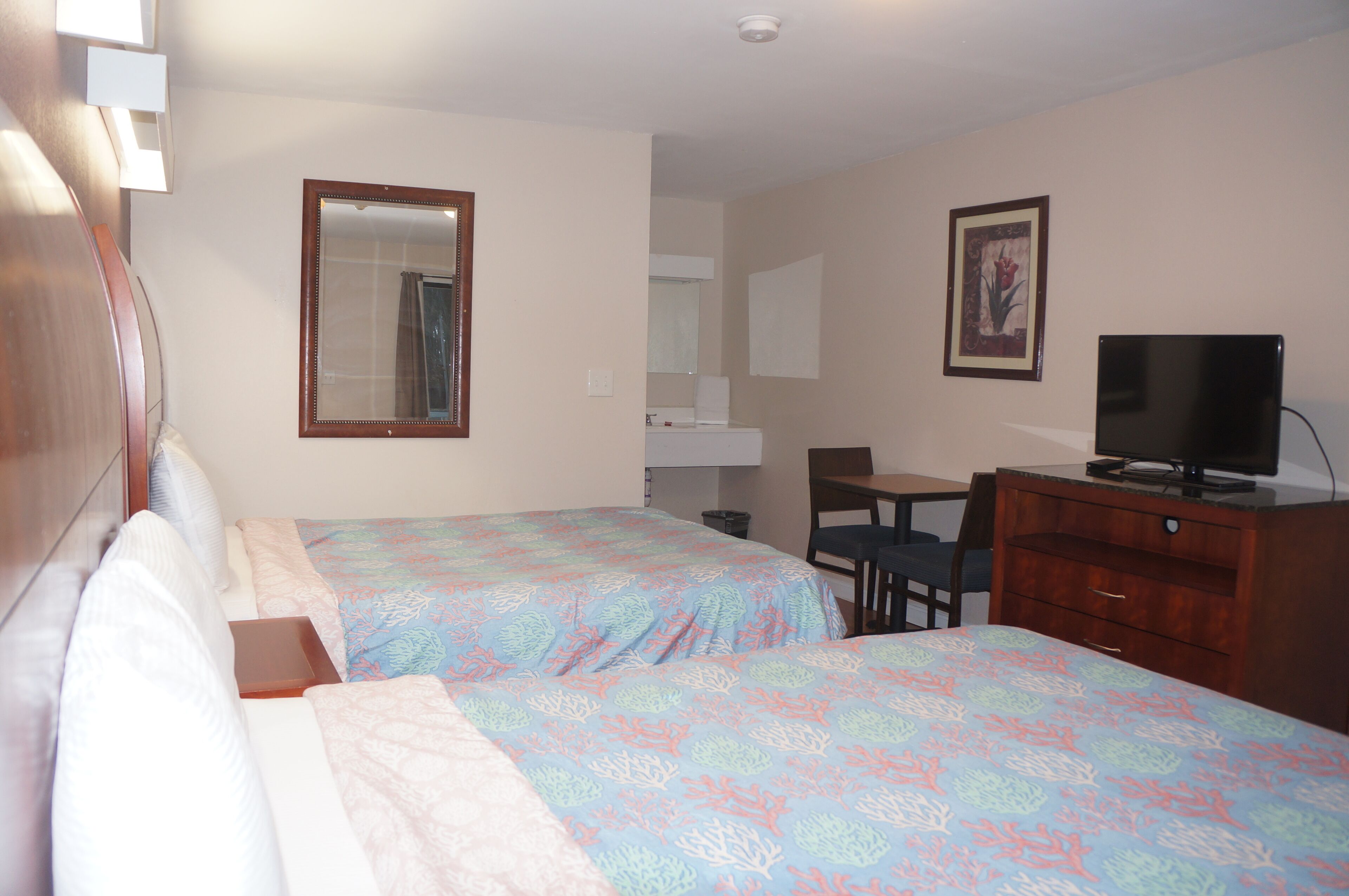 A hotel room with two beds, a desk, a chair, a television, and a bathroom visible in the background.