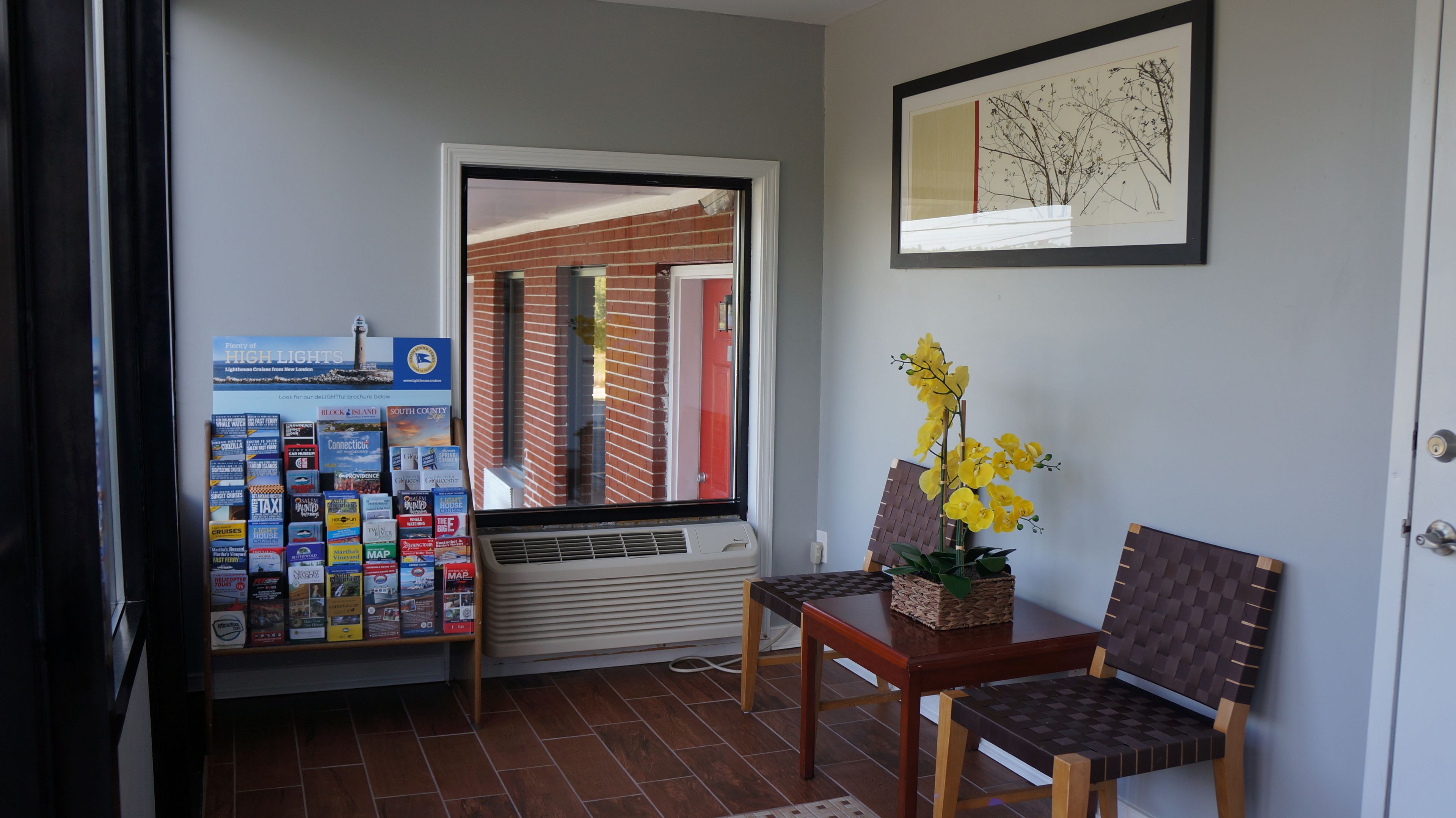 A reception area with a window view of a brick building, a framed artwork on the wall, and a table with chairs.