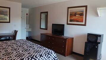 A hotel room with a bed, a dresser, a television, a microwave, a desk, and two framed pictures on the wall.