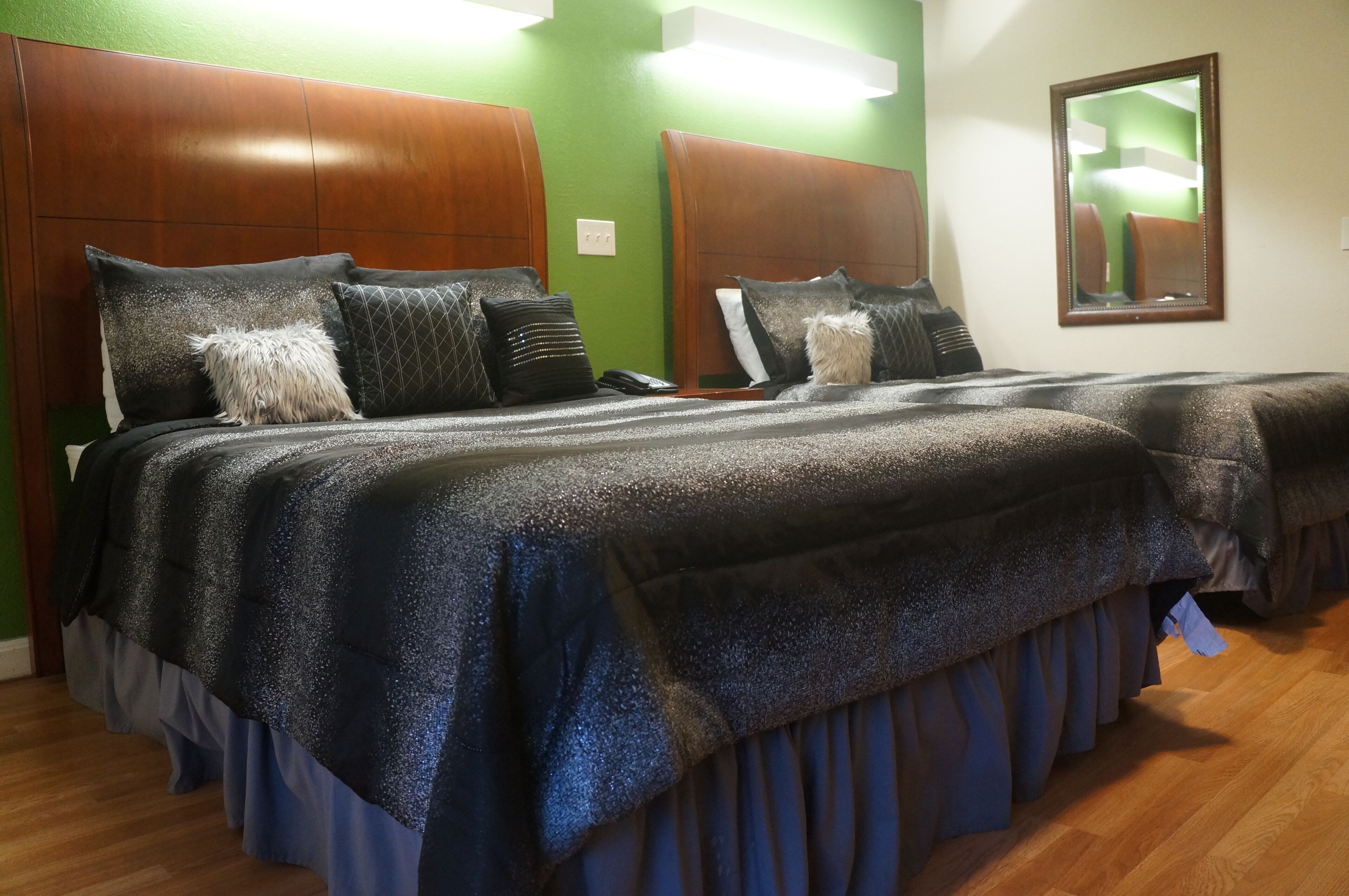 A hotel room with two beds, each with a headboard, a mirror, and a telephone on the nightstand.