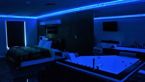 Un dormitorio moderno con una cama grande, una zona de estar independiente con bañera y un escritorio pequeño con silla.