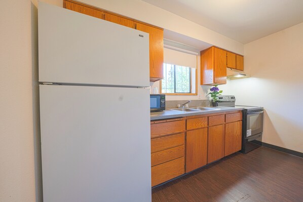 A kitchen with wooden cabinets, a refrigerator, a microwave, a stove, and a window.