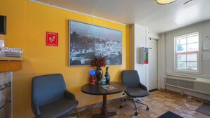 Un área de recepción con dos sillas, una mesa con una revista, un jarrón con flores, un cuadro de un gran paisaje urbano y un cartel de seguridad contra incendios.