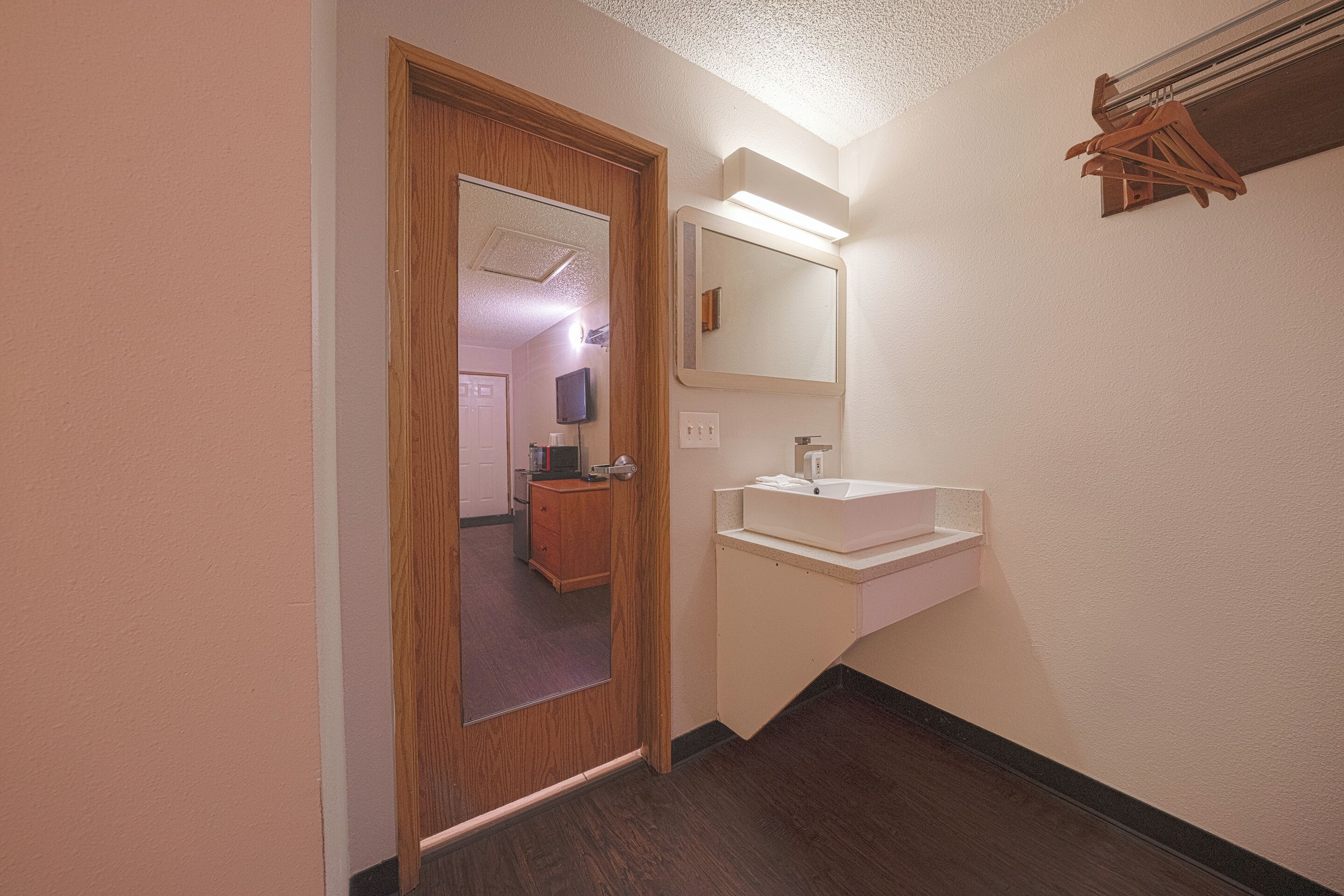 Un couloir étroit avec une porte en bois, un lavabo blanc et un miroir.