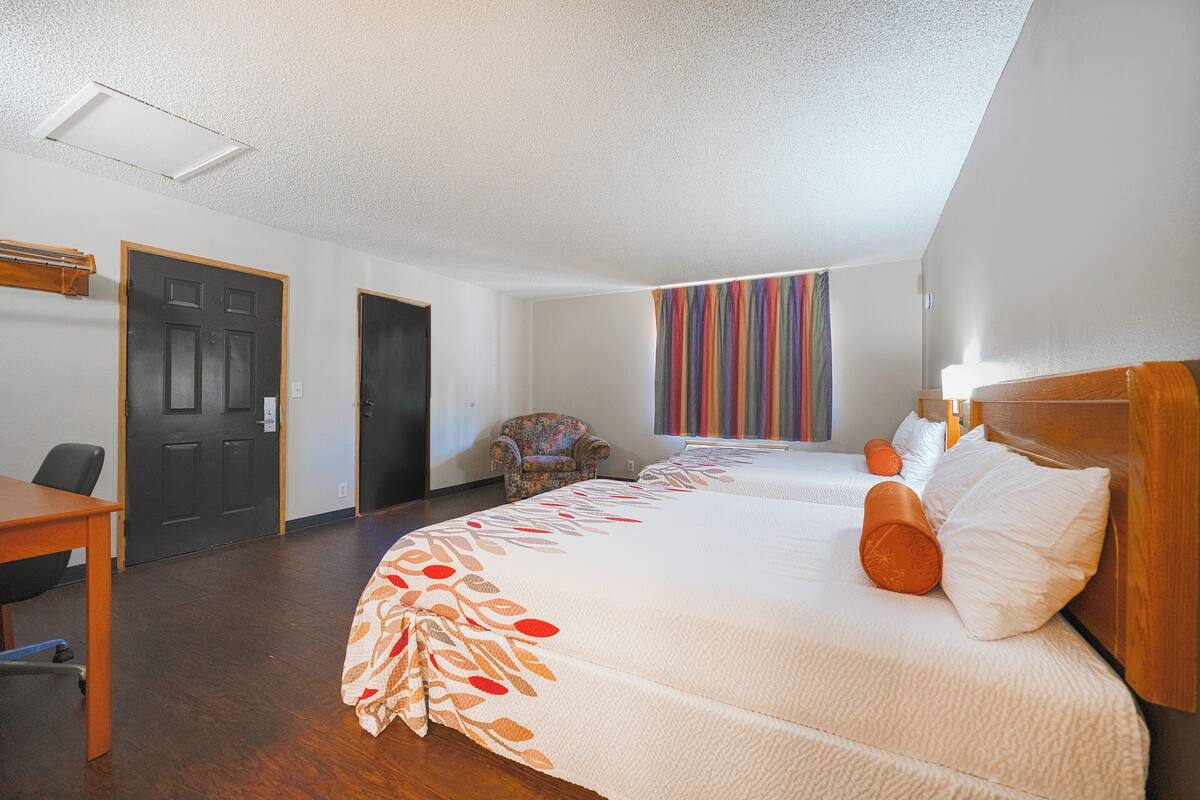 A hotel room with two beds, a desk, and a chair.