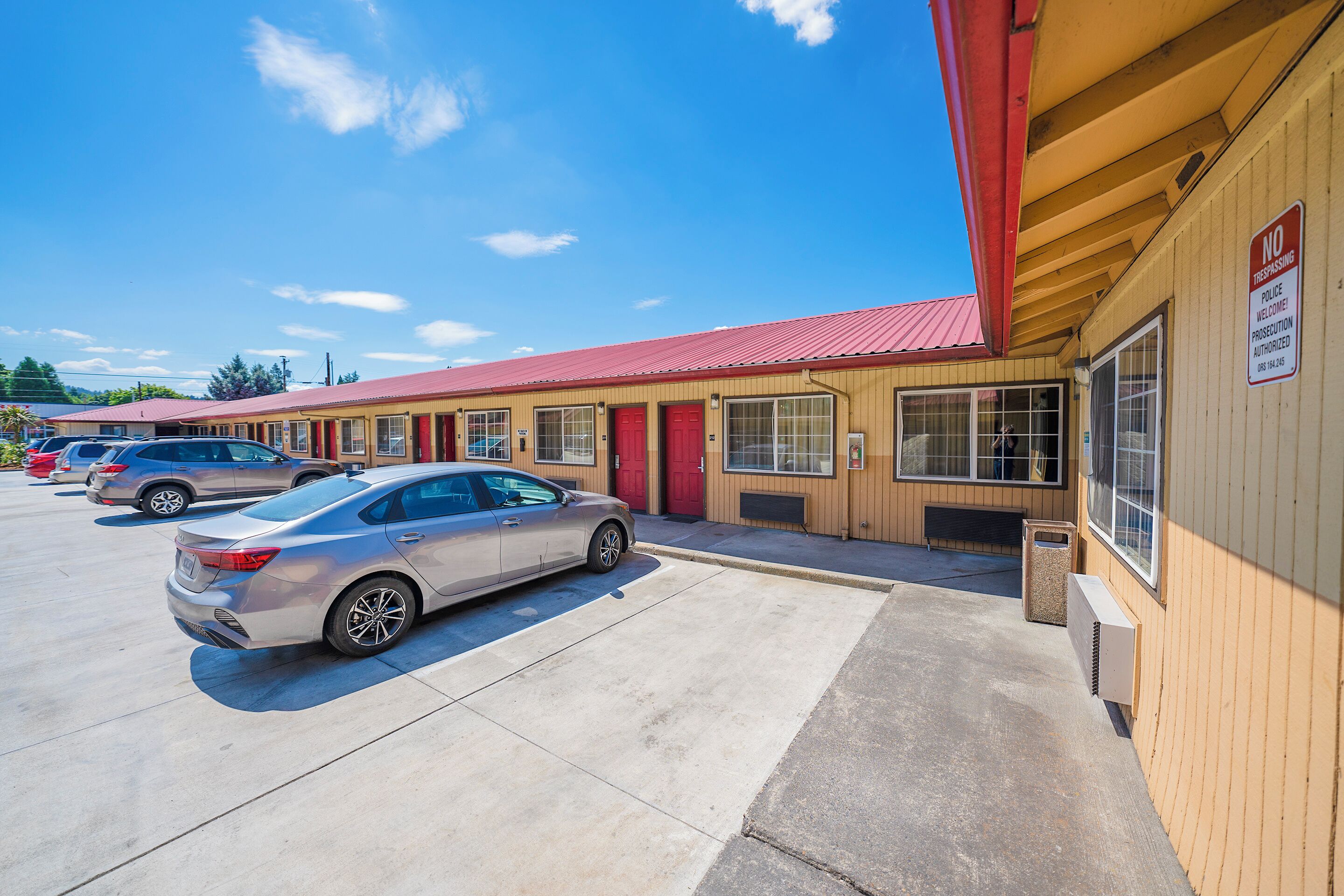 A motel with a red roof and beige walls, featuring a parking lot with several cars.