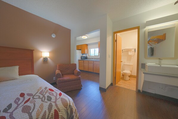 A hotel room with a bed, a chair, a bathroom, and a kitchenette.
