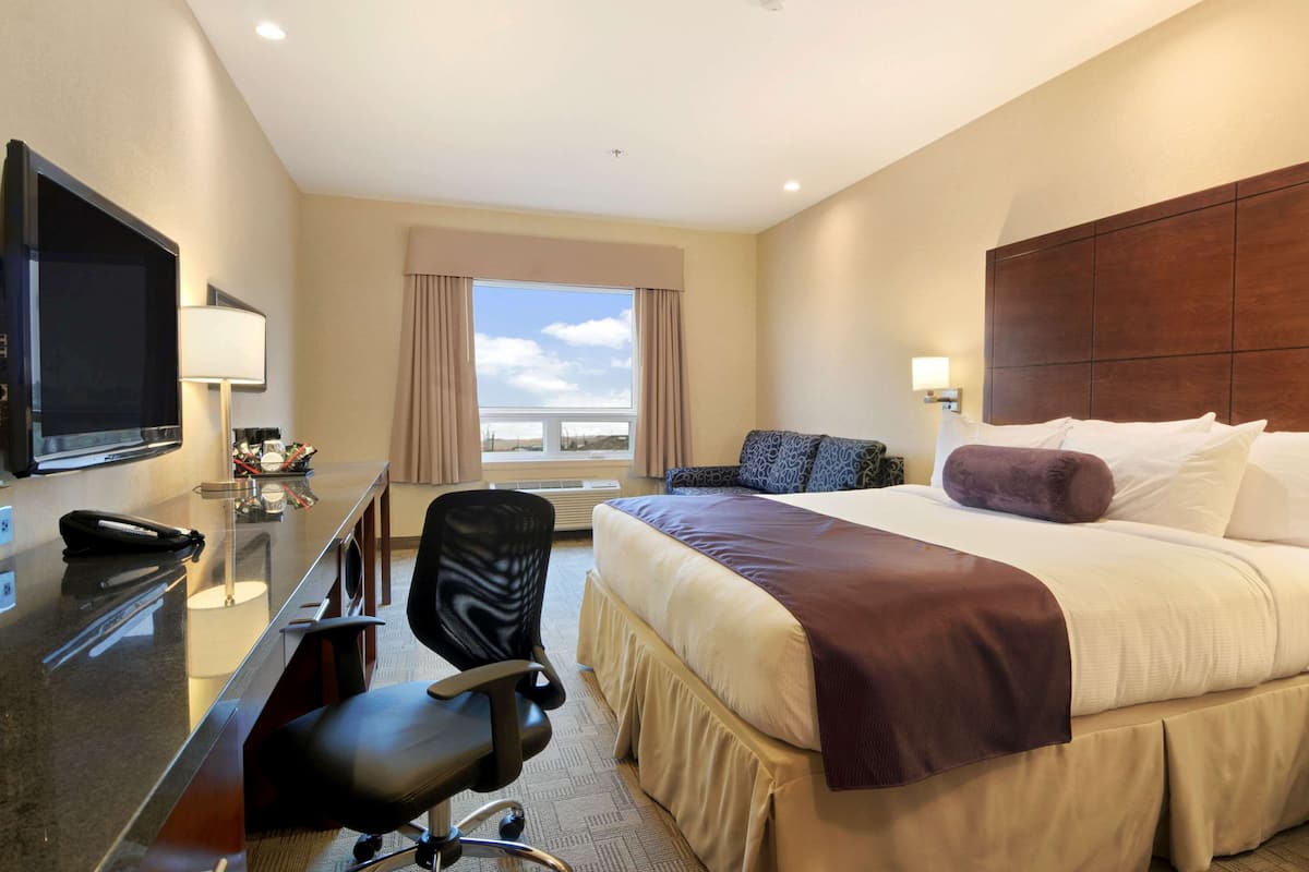 Habitación de hotel con una cama grande, un escritorio con computadora, una silla, televisor y ventana con cortinas.
