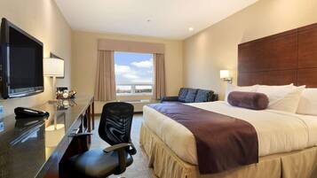 Habitación de hotel con una cama grande, un escritorio con computadora, una silla, televisor y ventana con cortinas.