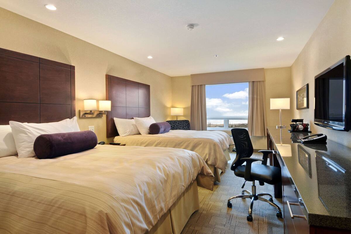 Habitación de hotel con dos camas, un escritorio, una silla, un televisor y un ventanal con vistas.