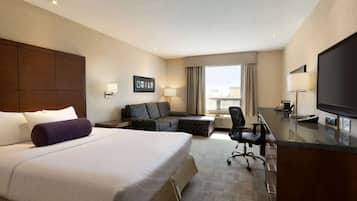 A hotel room with a large bed, a sofa, a desk, and a TV.
