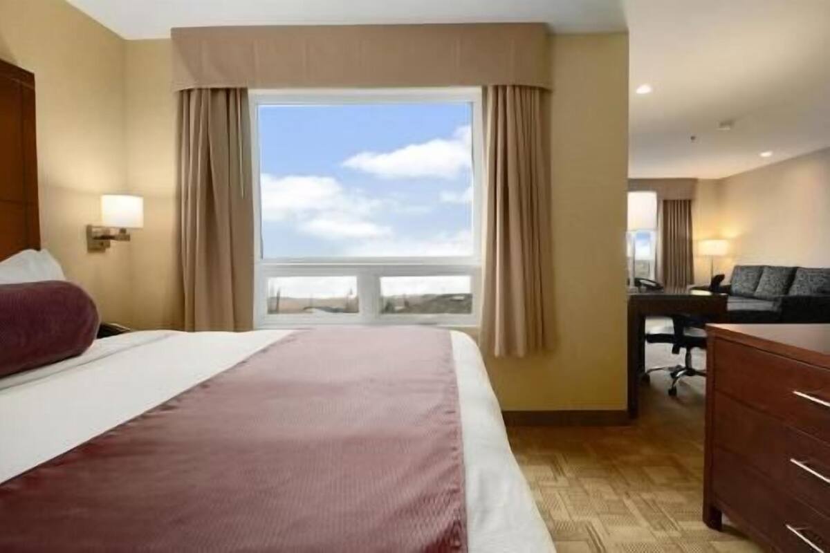 Habitación de hotel con cama, escritorio, silla y vista al cielo a través de la ventana.
