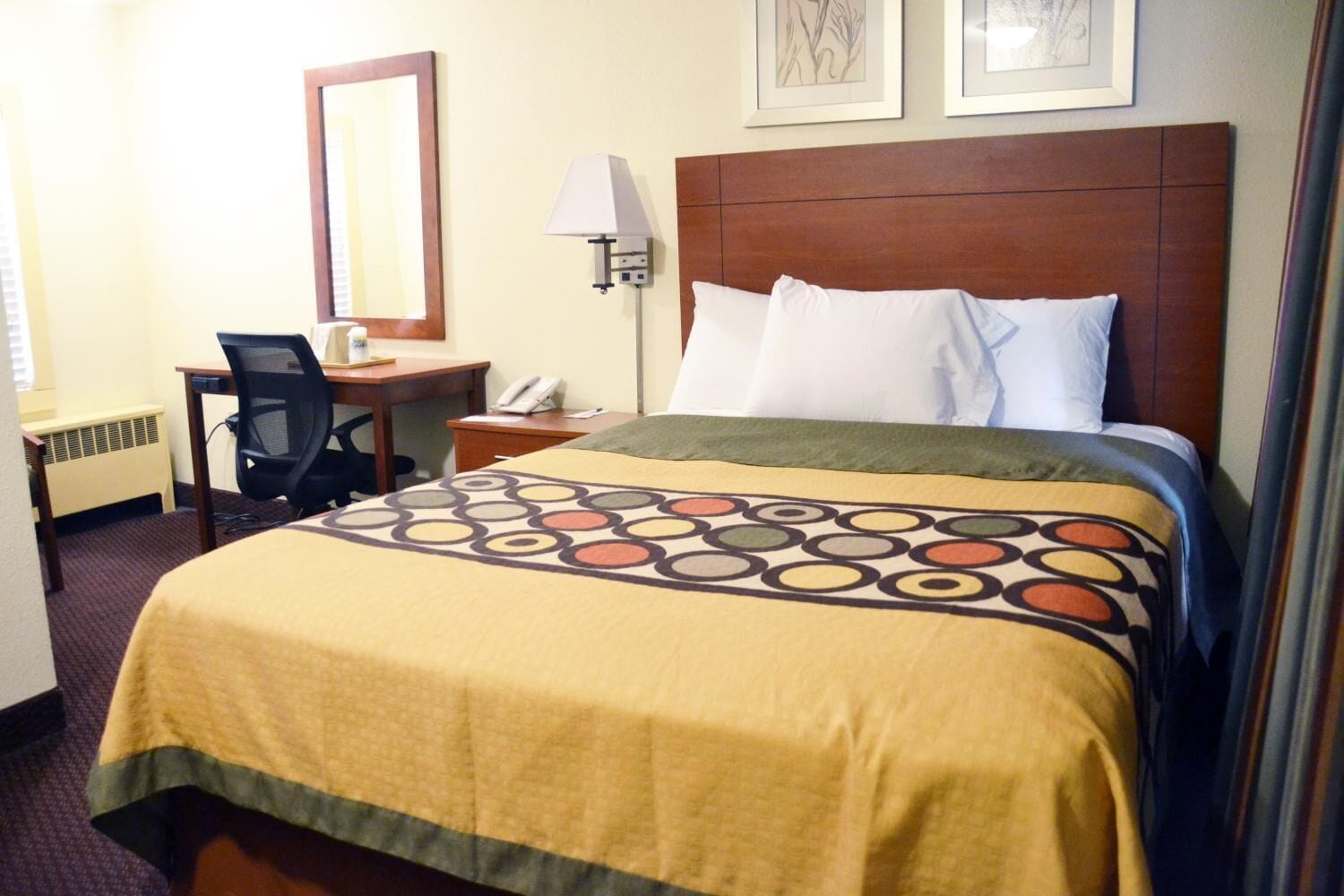 A hotel room with a bed, a desk, a chair, a lamp, and a mirror.