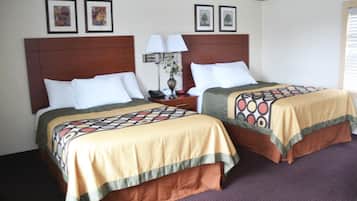 Una habitación de hotel con dos camas, cada una con una colcha estampada, cabecero de madera, mesita de noche con lámpara y cuadros en la pared.