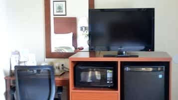 Een kleine hotelkamer met een houten bureau, een zwarte bureaustoel, een televisie, een magnetron en een koelkast.