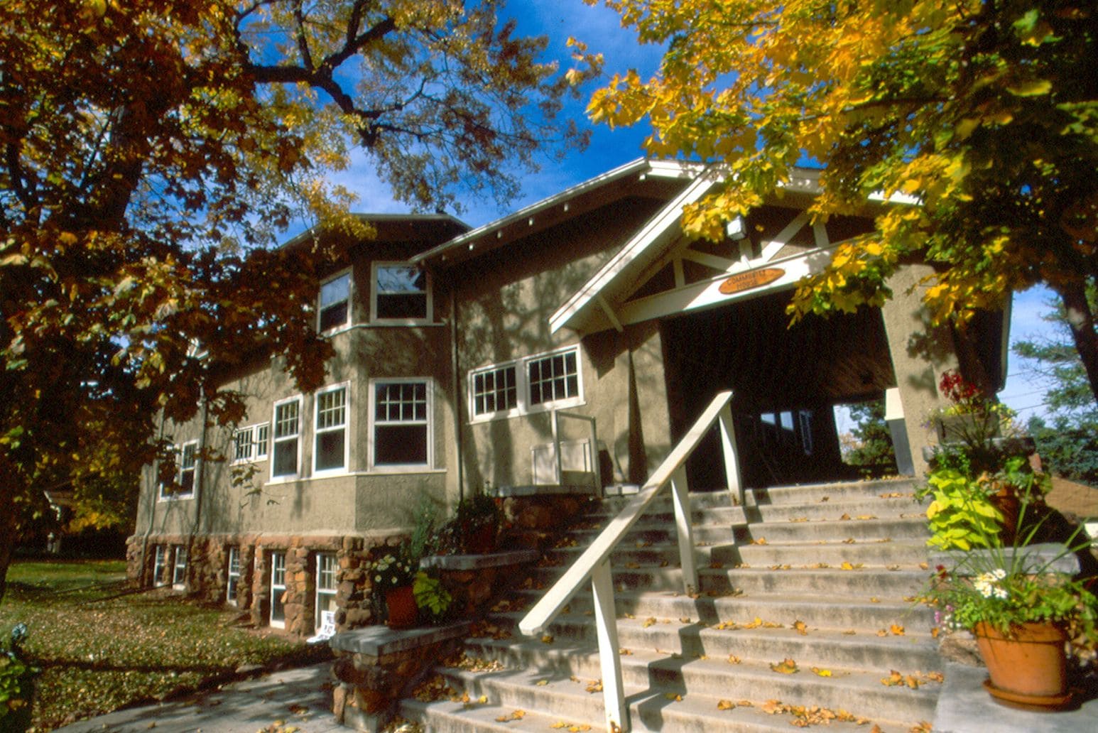 A two-story house with a stone facade, multiple windows, and a front porch with steps leading to a covered entrance.