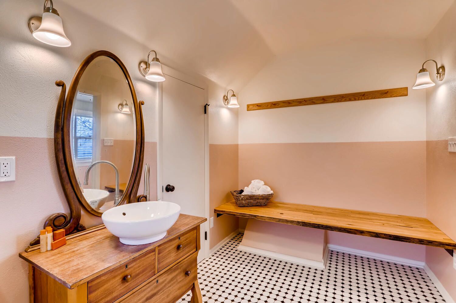 A bathroom with a wooden vanity, a large oval mirror, a white sink, and a shelf with towels.