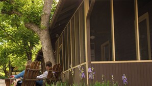 A wooden bench outside a building with large windows and a tree nearby. - Colorado Chautauqua (Boulder)