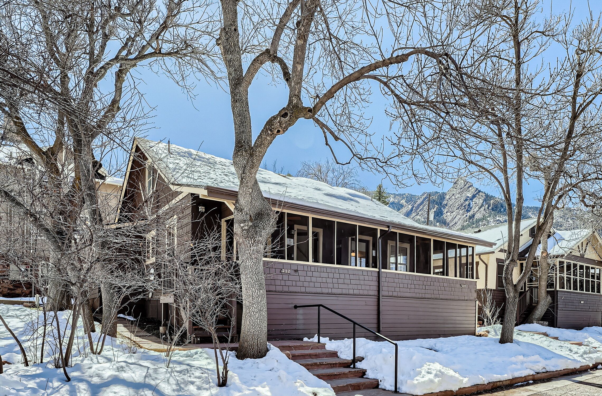 A two-story house with a snow-covered roof, a brick exterior, and a staircase leading to the entrance.