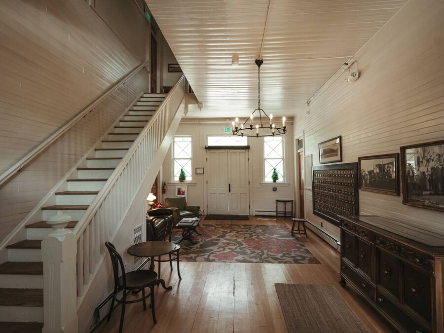 A spacious hallway with a wooden staircase, a chandelier, and a large wooden cabinet with framed pictures.