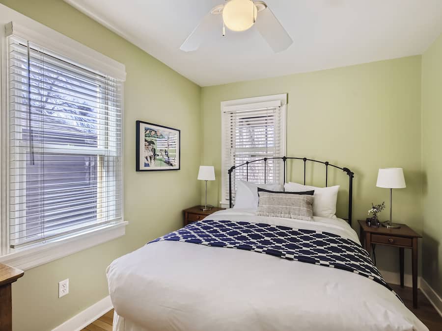 A bedroom with a bed, two nightstands, a ceiling fan, and two windows with blinds.