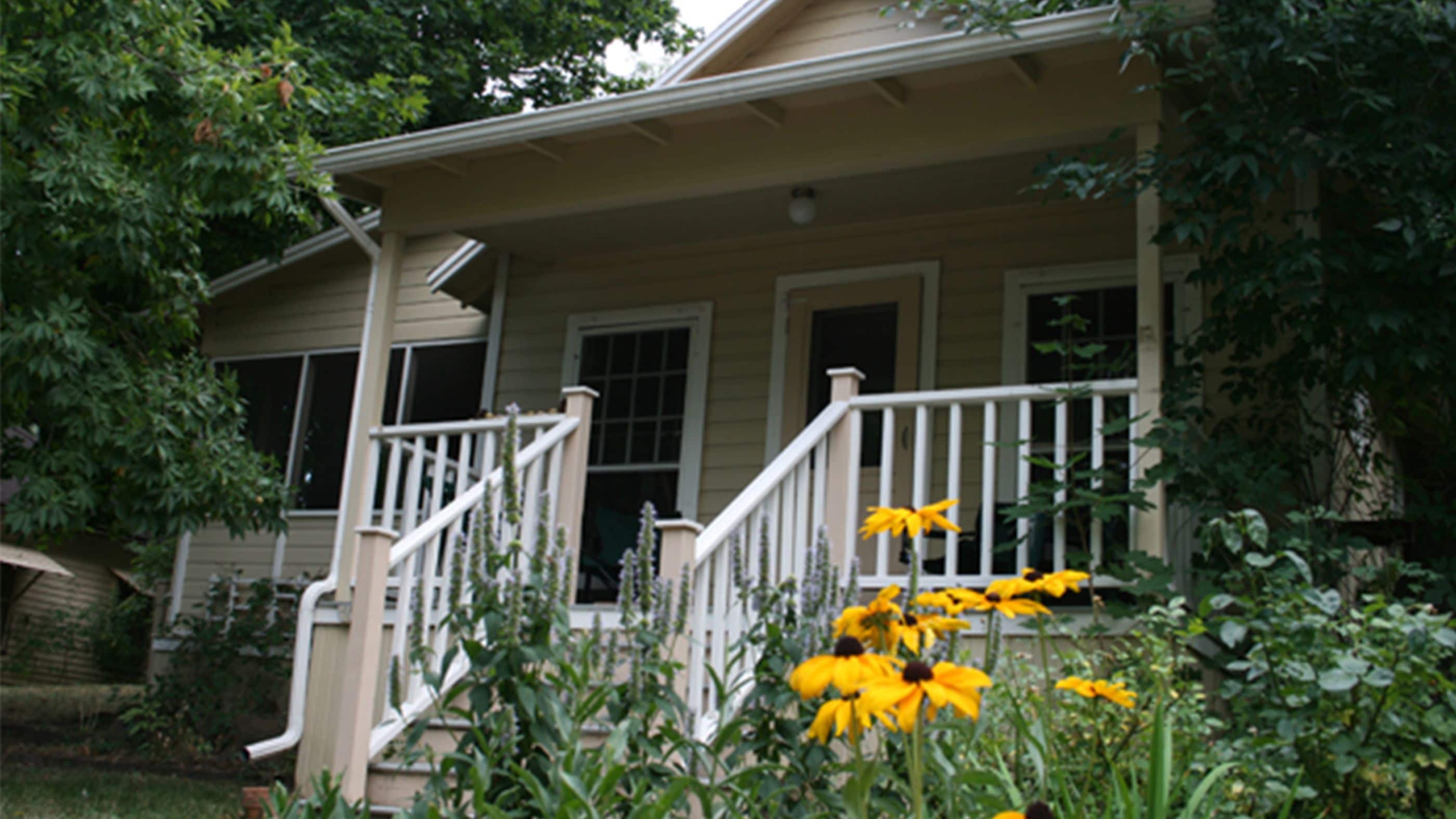 A two-story house with a porch, a staircase, and yellow flowers in the foreground.