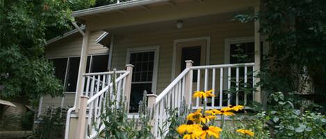 A two-story house with a porch, a staircase, and yellow flowers in the foreground.