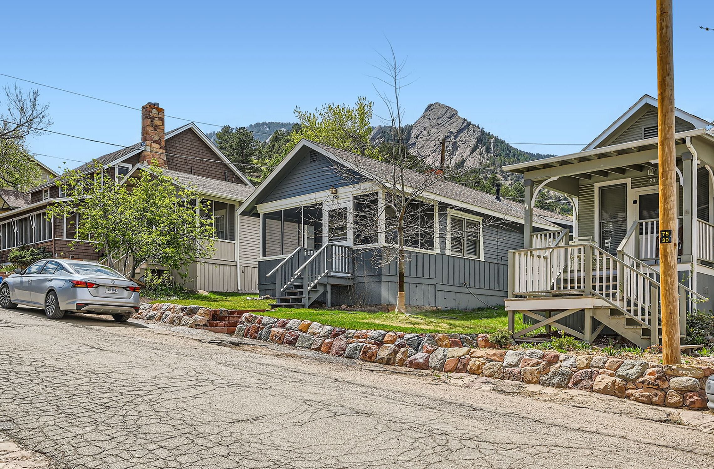 A row of single-story houses with a stone retaining wall, a car parked in front, and a mountain in the background.
