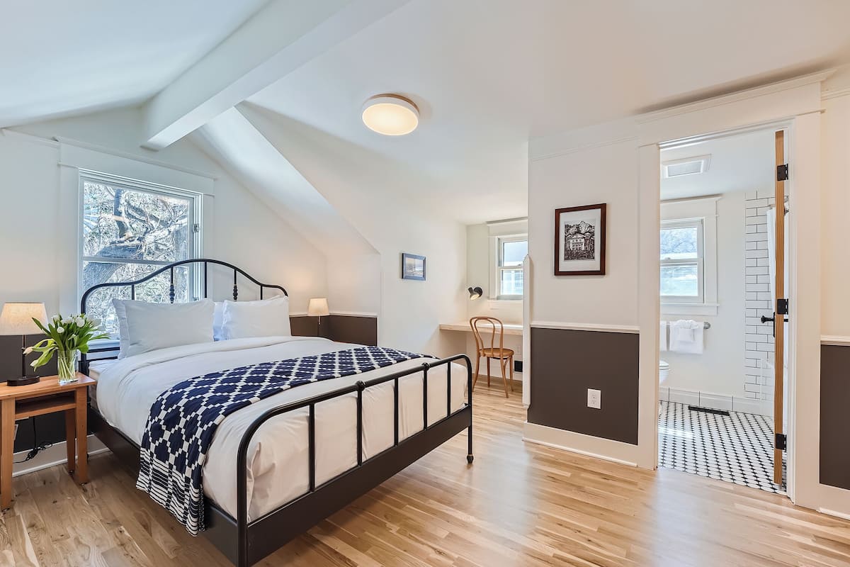 A bedroom with a bed, bedside table, lamp, and a view of the outside.