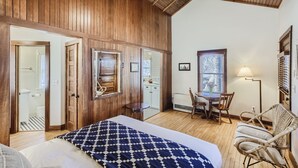 A room with a wooden ceiling, a bed with a patterned blanket, a dining table with chairs, and a lamp. - Colorado Chautauqua (Boulder)