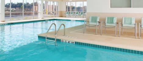 En inomhuspool med kristallklart blått vatten, en skylt som förbjuder dykning och en sittplats med stolar och handdukar.