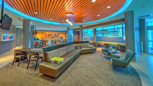 A modern lobby with a curved wooden ceiling, seating areas, and a visible restaurant in the background. - SpringHill Suites by Marriott Macon (Macon)