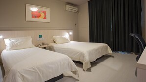 Une chambre d’hôtel avec deux lits, un bureau, un téléphone et un tableau au mur.