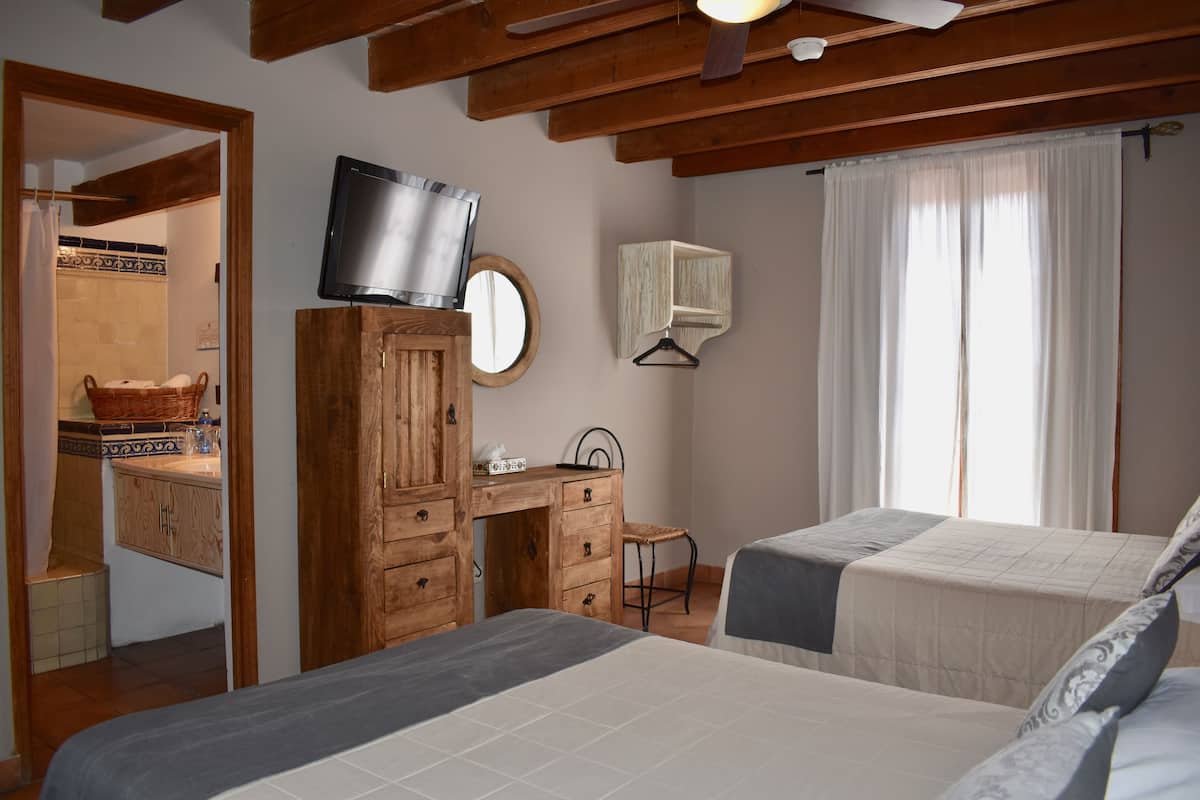 A bedroom with two beds, a wooden desk, a television, a mirror, and a window with curtains.