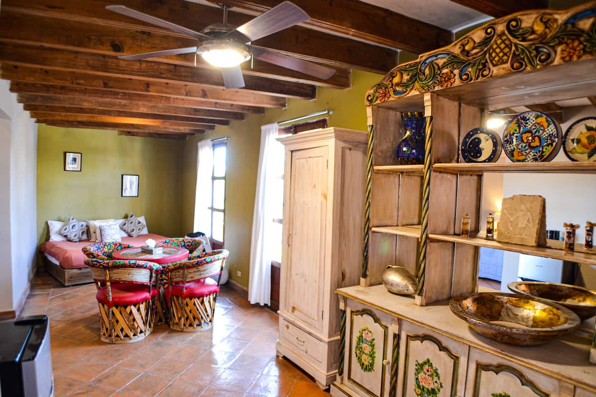 A room with a bed, a dining table with chairs, a cabinet, and decorative plates on shelves.