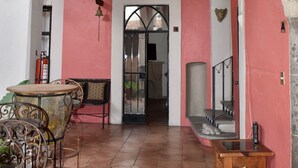 A corridor with a red wall, white arches, a tiled floor, a metal table, and a bench. - Hotel Ana Catalina & Suites (San Miguel de Allende)